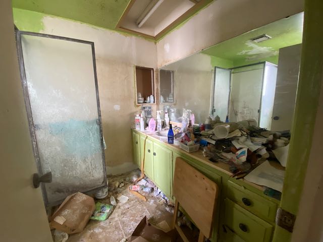 ごみ屋敷の内部。写真はバスルームの洗面台だがものが置けないくらい紙やプラスチックが重なっておかれている。シャワーのドアも汚れている